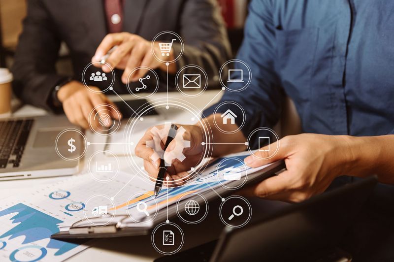 Photo; two people at a table; laptop and clipboard; in the foreground graphic elements on the subject of project administration