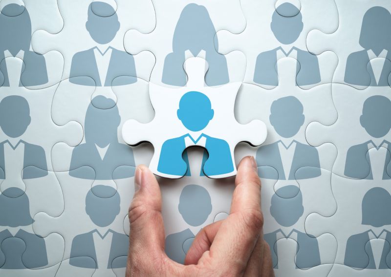 Foto; eine Hand setzt den letzten Stein eines Puzzles; Puzzlesteine mit Grafiken von Business-Personen