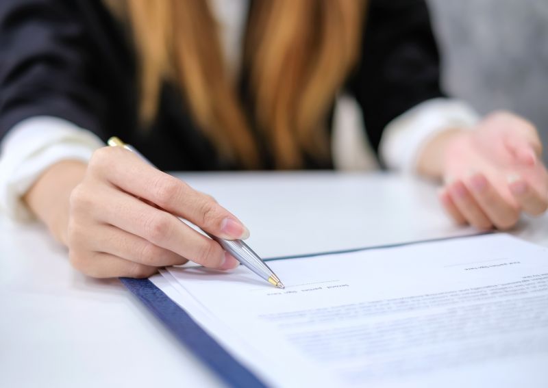 Photo; a person points with a pen to the signature in a contract