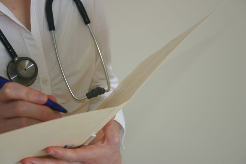 Photo; female doctor with stethoscope and patient file, she writes with a pencil