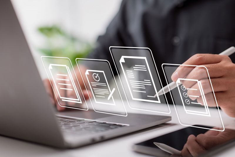 Photo; A person in front of a laptop; in the foreground icons of contracts and documents.