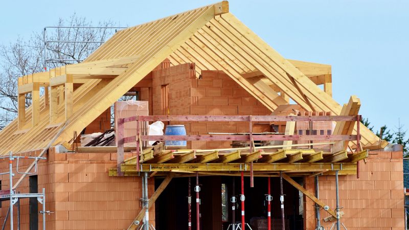 Bild mit Rohbau eines Einfamilienhauses, offenes Dach, Baugerüst hält Stahlträger des Balkons