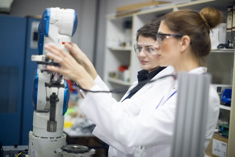 Foto; zwei Frauen mit weißem Kittel an einem technischem Gerät